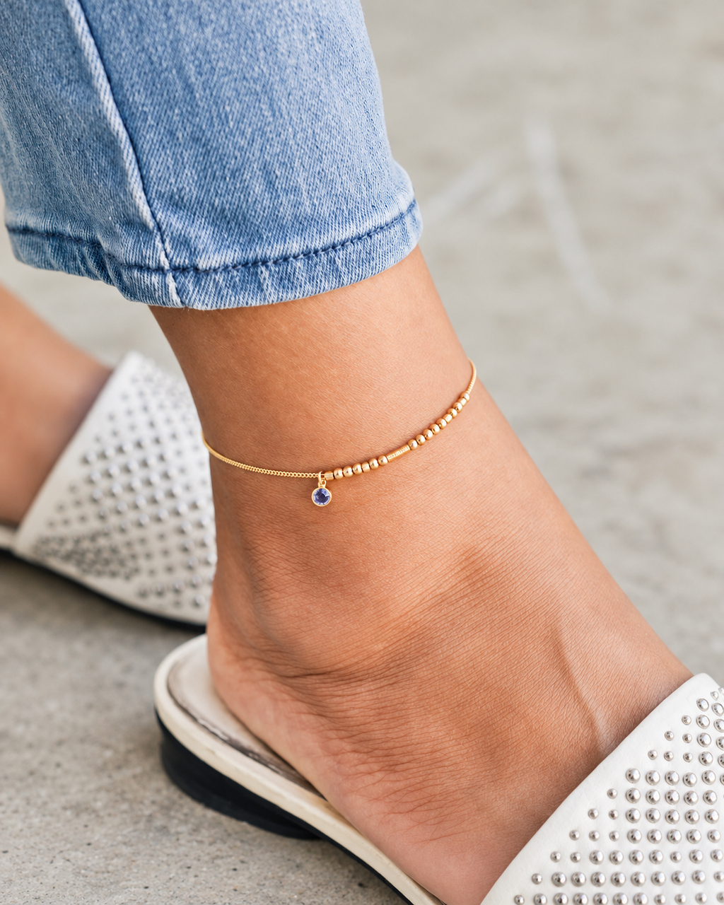 Detail of a custom-designed gold Morse code anklet spelling a name, paired with a small birthstone charm on a delicate chain in natural lighting