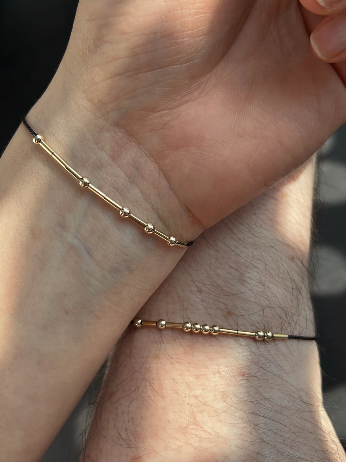 A couple holding hands while wearing custom matching thread Morse code bracelets with secret personalized initials.