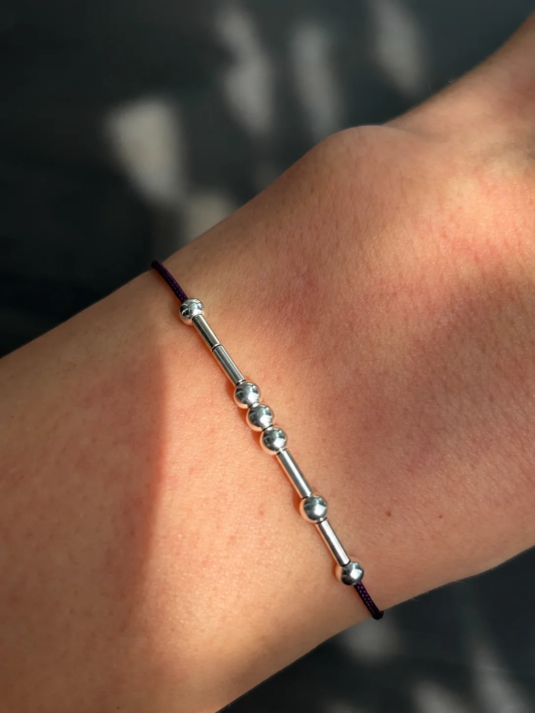 Minimalist custom Morse code cord bracelet featuring anti-tarnish rhodium silver beads representing personalized 5 to 6 letter initials on a wrist in sunlight.