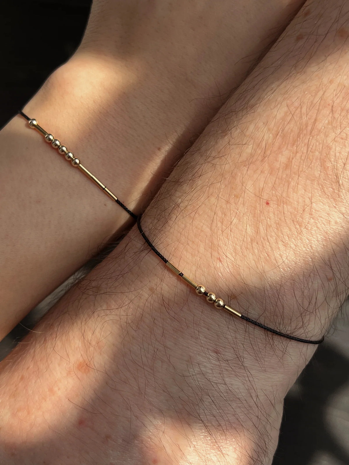 Male and female wrists side-by-side displaying personalized Morse code couple bracelets crafted with adjustable black cord and gold accents.