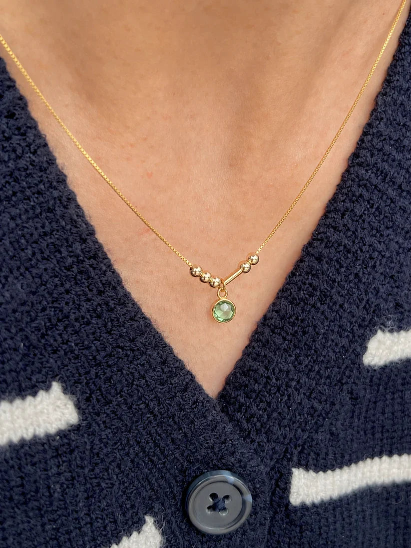 A minimalist 22K gold Morse code necklace featuring couple's initials and a bright green bezel-set anniversary birthstone charm[cite: 11].