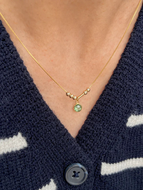 A minimalist 22K gold Morse code necklace featuring couple's initials and a bright green bezel-set anniversary birthstone charm[cite: 11].