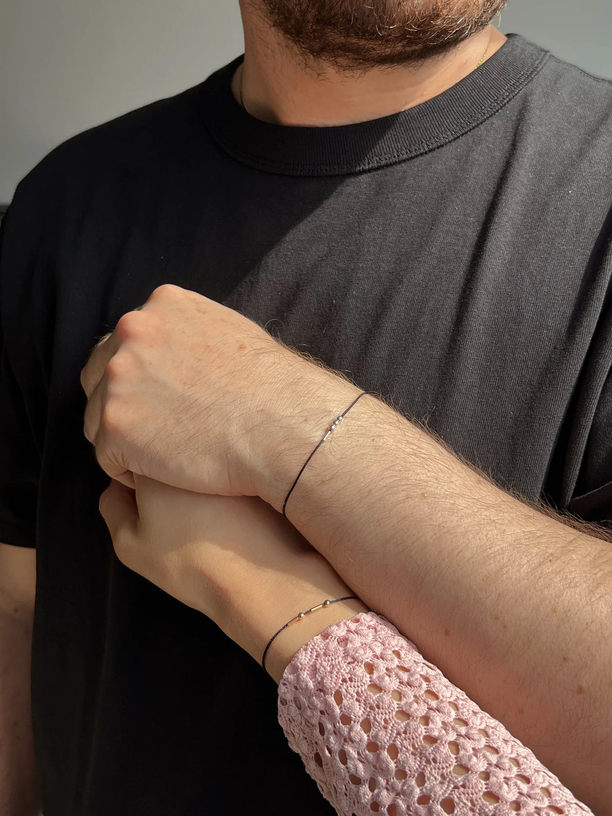 Close-up of matching personalized Morse code cord couple bracelets featuring 22K gold geometric beads on minimalist black thread.