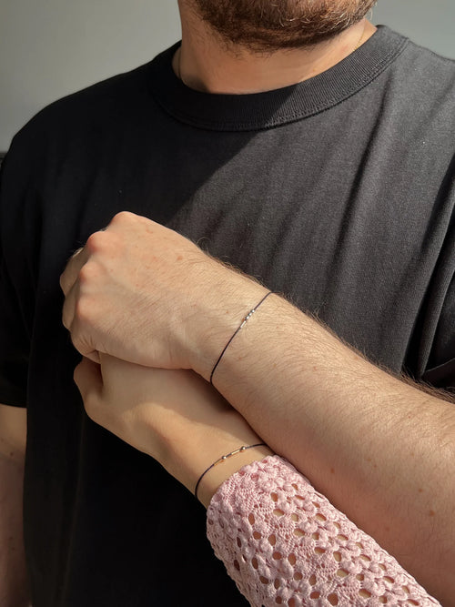 Close-up of matching personalized Morse code cord couple bracelets featuring 22K gold geometric beads on minimalist black thread.
