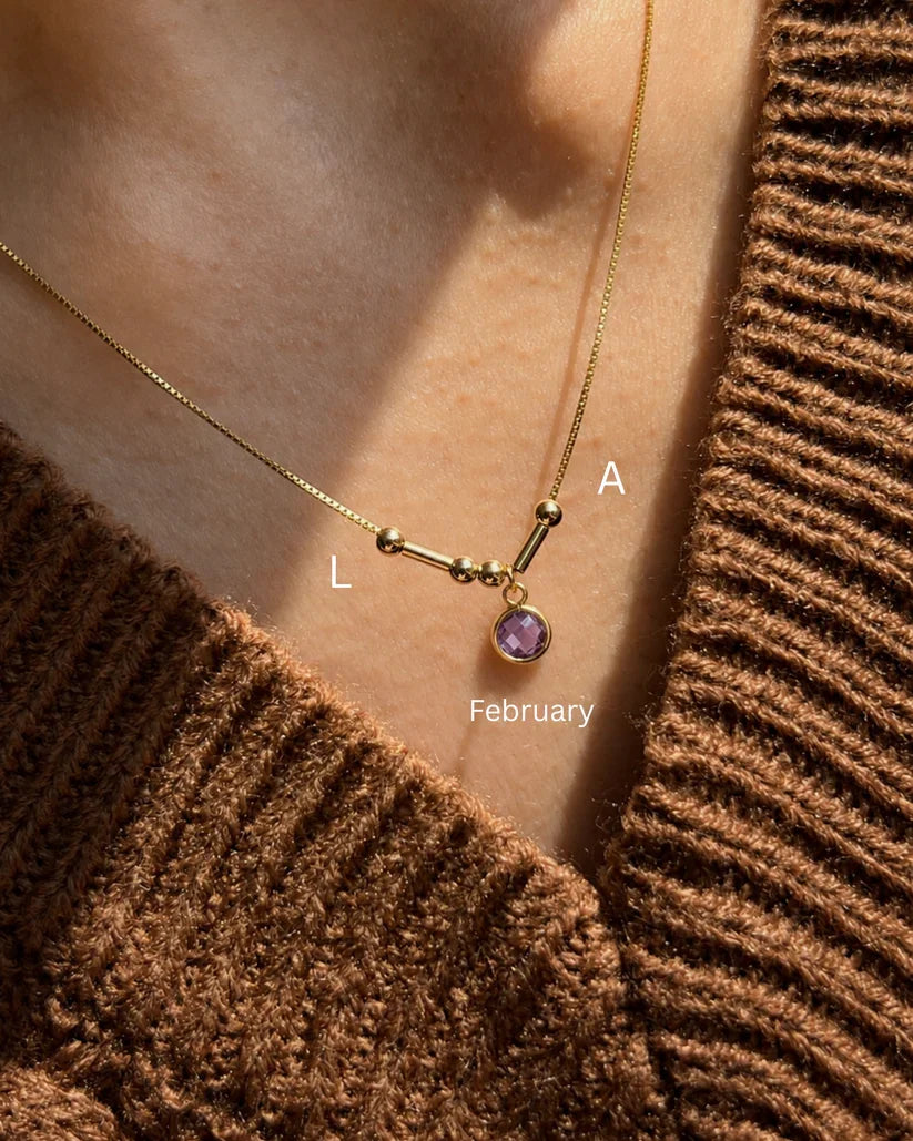 A custom couple's Morse code necklace featuring the initials L and A, beautifully connected by a purple February birthstone pendant[cite: 10].